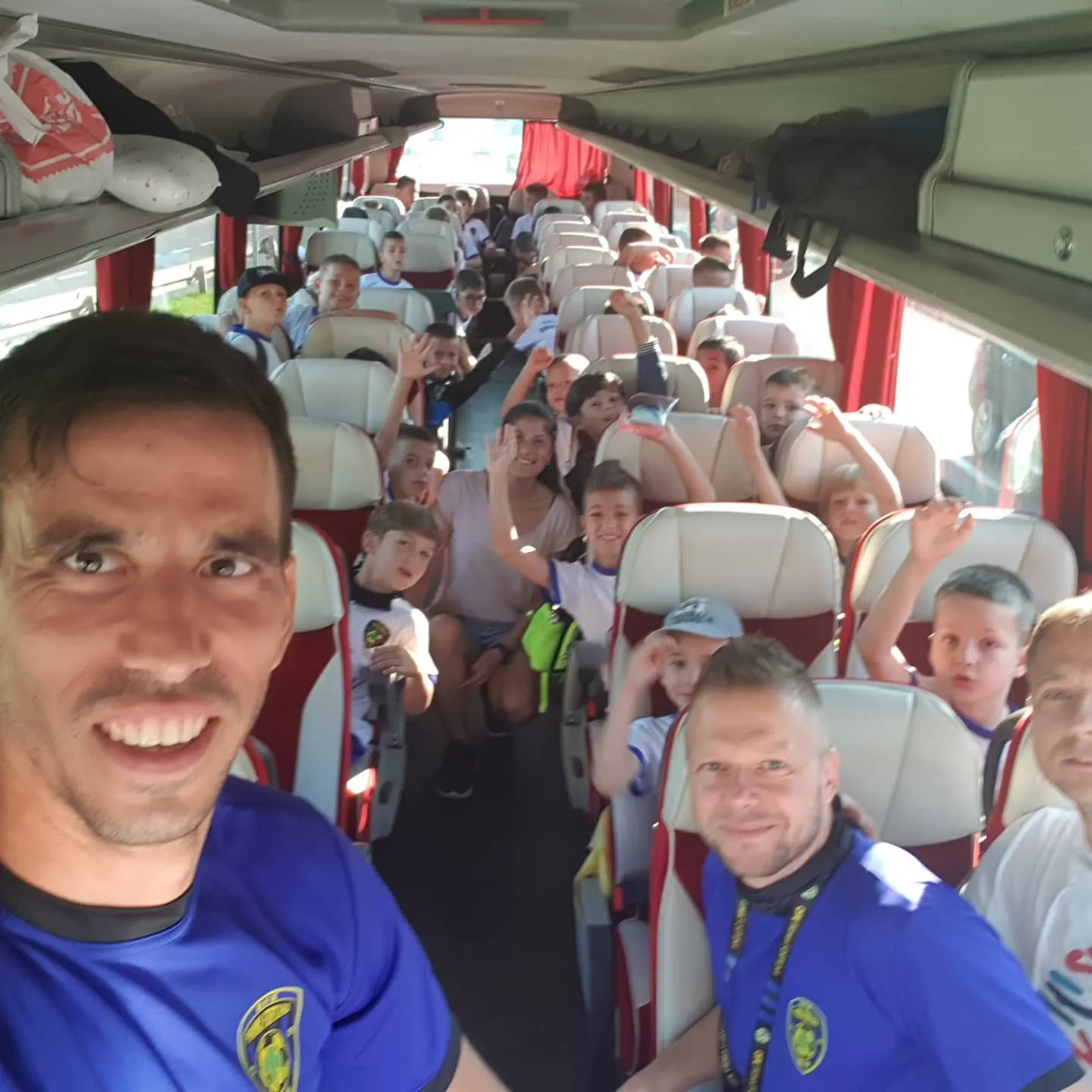 Deca i treneri mašu u autobusu, snimljeno iz prvog reda