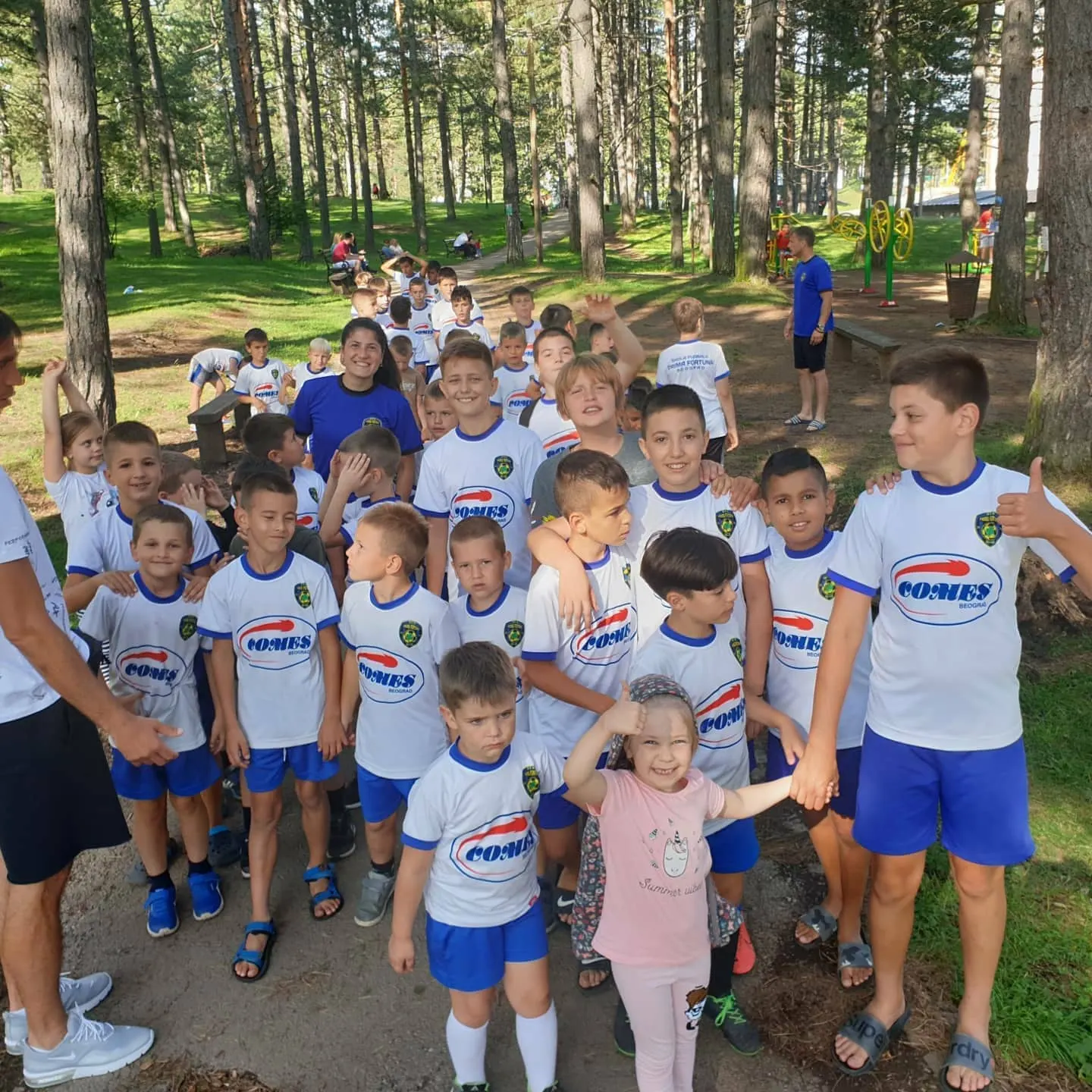 Velika grupa dece u klupskim majicama među borovima