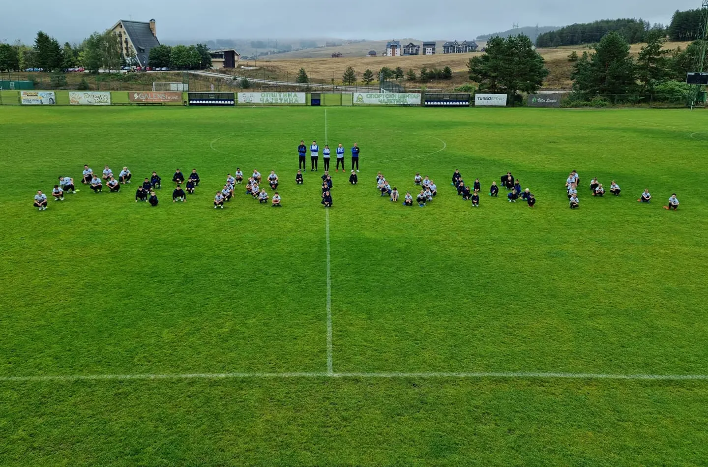 Deca sede na stadionu i slažu natpis, treneri stoje u sredini