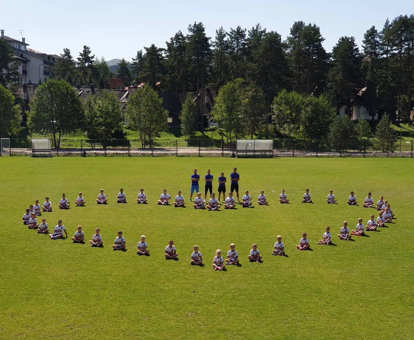 Deca sede na travi u obliku srca, treneri stoje u sredini
